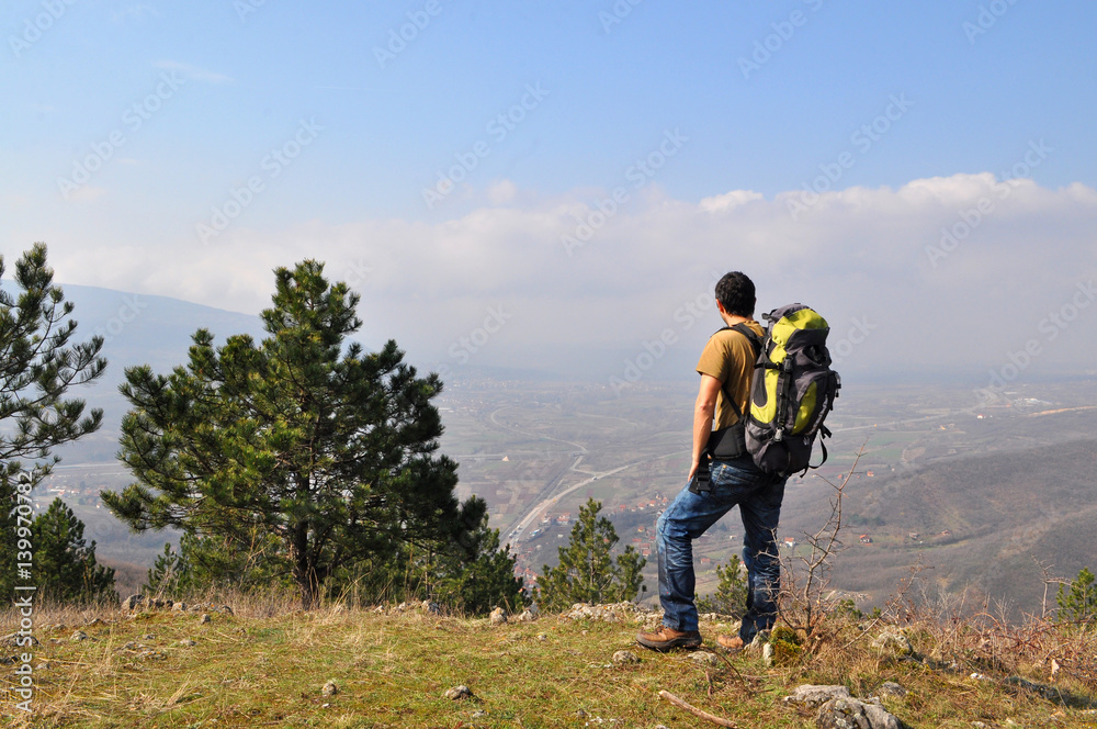 Young man with backpack standing on top of the hill over the city