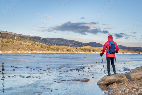 hiker at shore of frozen mountain lake