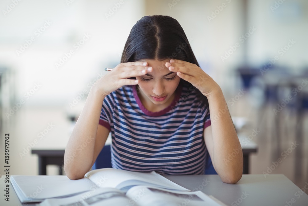 Fototapeta premium Attentive schoolgirl doing homework in classroom