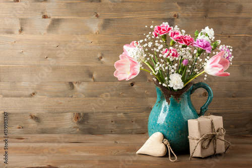 Fresh flowers in jug, gift box and heart on wooden background