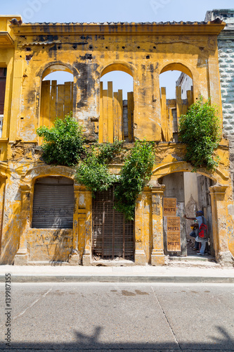 Fototapeta Naklejka Na Ścianę i Meble -  CARTAGENA, COLOMBIA - MAY 11: An unidentified man peers out of a doorway of a bright yellow building in Cartagena, Colombia on May 11, 2016.