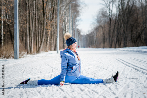 Beautiful young girl stretches on a sports field in winter against a background of deciduous forest. Winter sports concept photo