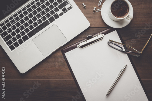 view from above. brown wooden office table with cup of coffee, notepad and laptop computer