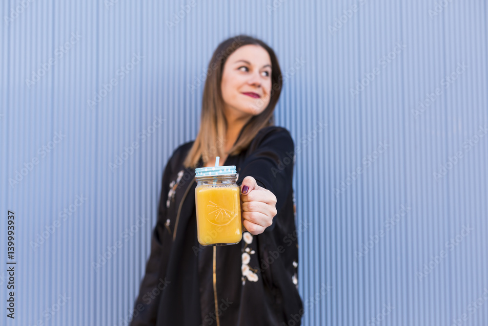 Fashion pretty woman model with fresh fruit juice cup wearing sunglasses and black jacket over colorful blue background. Fashion pretty woman model with fresh fruit juice cup wearing sunglasses and black jacket over colorful blue background.