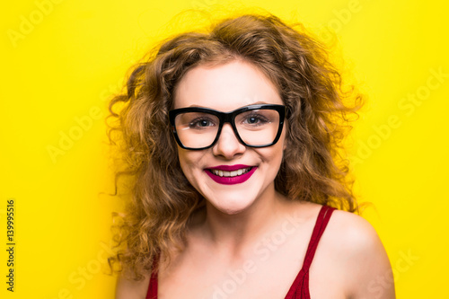 Beauty portrait of young girl with curly hairstyle. Girl posing on yellow background, looking at camera, smiling. Studio shot.