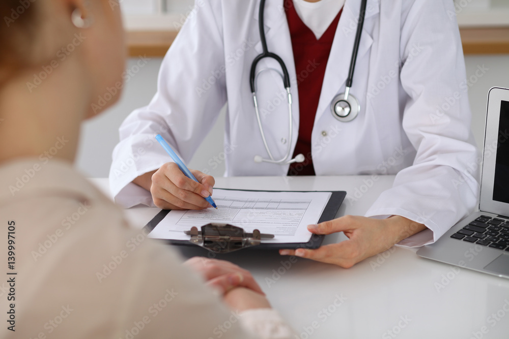 Close up of a female doctor filling up an application form while consulting patient. Medicine and health care concept Close up of a female doctor filling up an application form while consulting patient. Medicine and health care concept