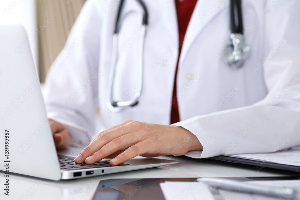 Close up of unknown female doctor typing on laptop computer while sitting at the table. Medical staff, compulsory work concept Close up of unknown female doctor typing on laptop computer while sitting at the table. Medical staff, compulsory work concept