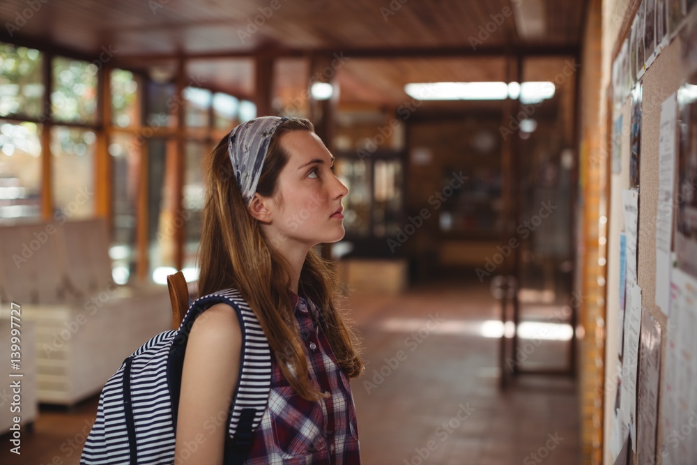 Schoolgirl reading notice board in corridor