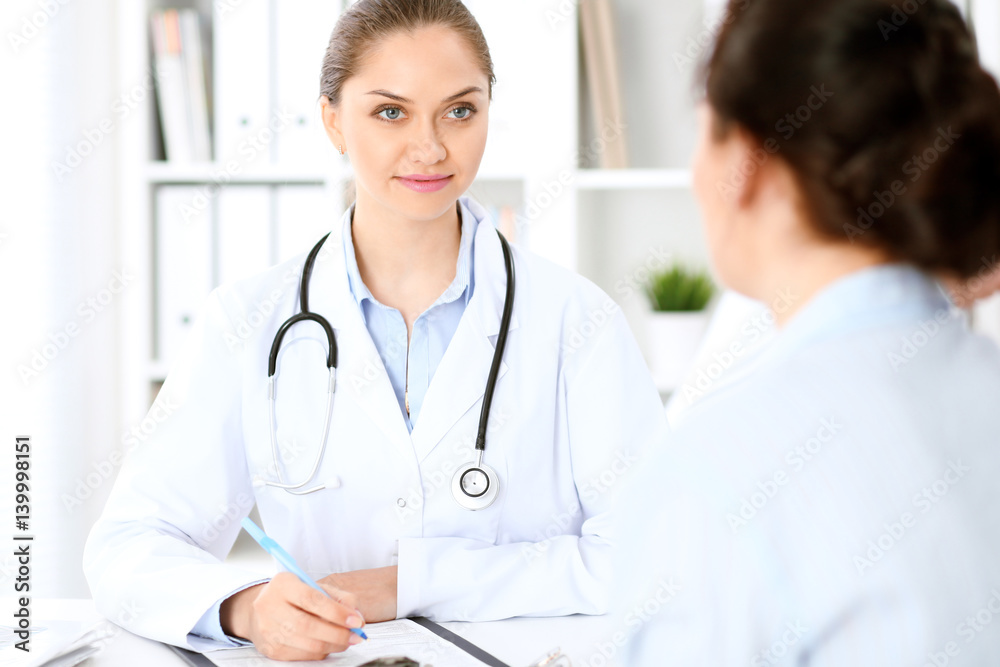 Friendly smiling doctor and patient sitting at the table. Very good news and high level medical service concept. Friendly smiling doctor and patient sitting at the table. Very good news and high level medical service concept.