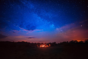 Camping fire under the amazing blue starry sky with a lot of shining stars and clouds. Travel recreational outdoor activity concept.