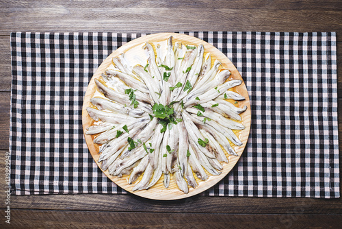 Anchovies with olive oil and vinegar on a wooden plate on a black and pink tablecloth next to a fork. Food.