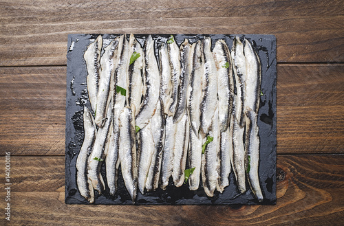 View from above of anchovies with olive oil and vinegar on a slate dish on a brown wooden table. Food Horizontal shoot.