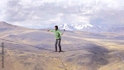 Slackliner balancing on tightrope between two rocks, Snowy mountains of the Huascaran park on the background, Peru. Slow motion photo