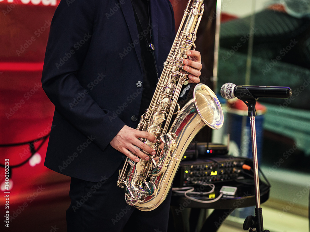Obraz premium Gold saxophone with specks on it in male hands in the red background.Hands of musician playing alto saxophone, closeup,Hands of groom play on saxophone,jazz music concept