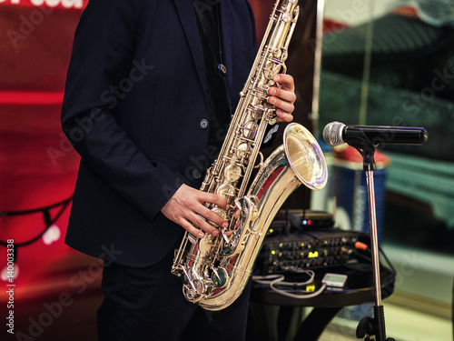 Photography Gold saxophone with specks on it in male hands in the red background