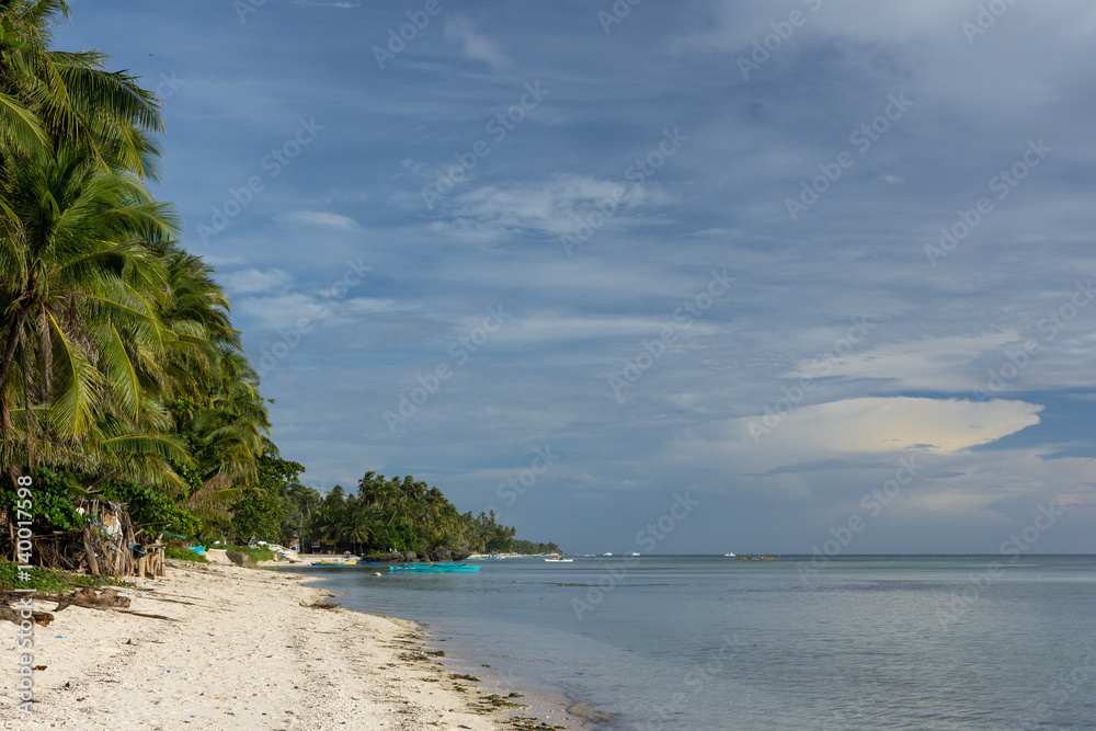 Beautiful palm tree lined white sand beach with calm clear sea and a build up of greying clouds.