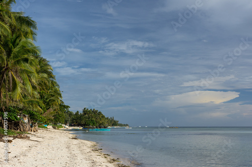 Beautiful palm tree lined white sand beach with calm clear sea and a build up of greying clouds. © phil