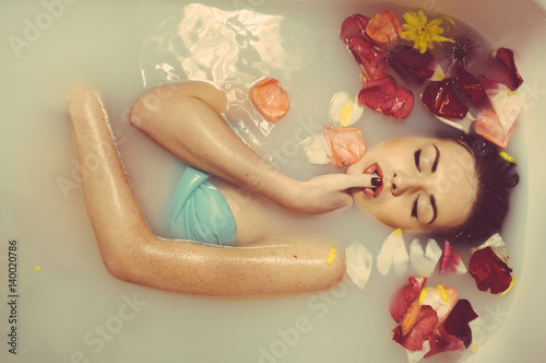 Beautiful sexy young woman having bath with flower petals