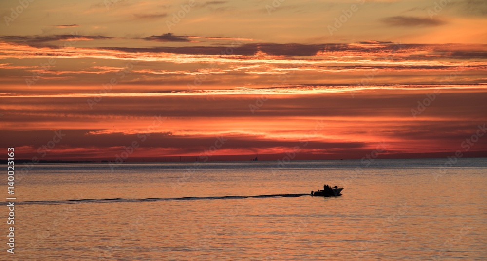 silhouette of boat underneath colorful sky at sunrise in summertime