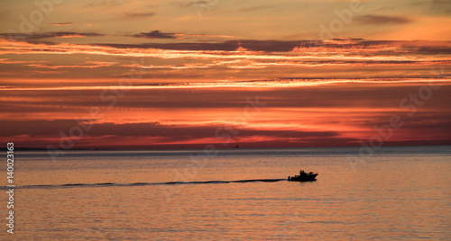 silhouette of boat underneath colorful sky at sunrise in summertime © Jazz