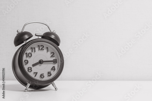 Closeup alarm clock for decorate show a quarter past eight o'clock or 8:15 a.m.on white wood desk and cream wallpaper textured background in black and white tone with copy space