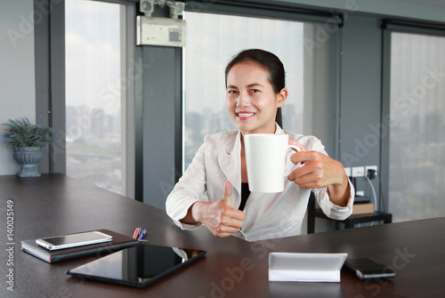 Young businesswoman sitting at the table on workplace in office with laptop computer drinking a coffee