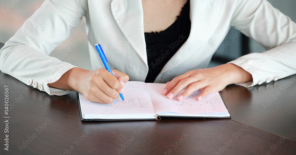 Close up young businesswoman sitting at the table on workplace in office and writing Close up young businesswoman sitting at the table on workplace in office and writing