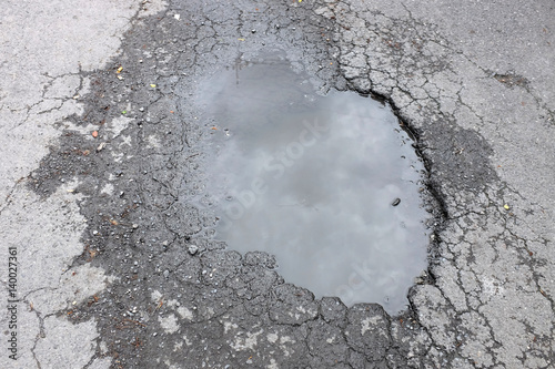 Tablou pe pânză The bad asphalted road for cars with a big pothole filled with water