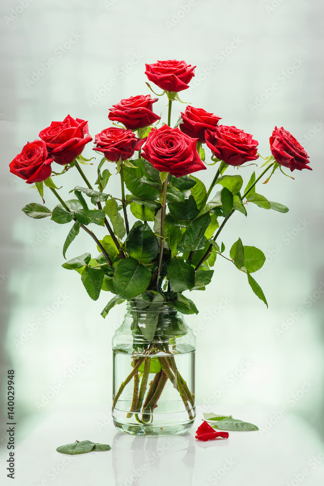 Fototapeta premium Bouquet from scarlet magnificent roses in bank with water on a light surface