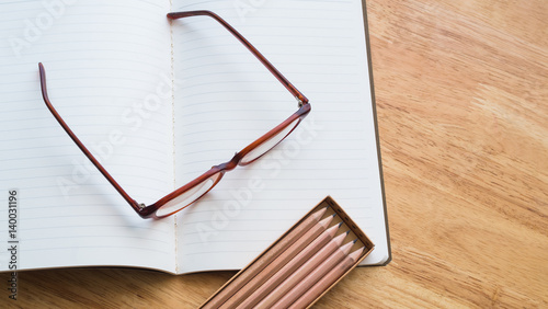 Glasses, pencil box and opened notebook on wooden table from top view point
