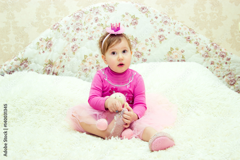 Charming little girl is sitting on the bed with a toy and is having fun playing Charming little girl is sitting on the bed with a toy and is having fun playing