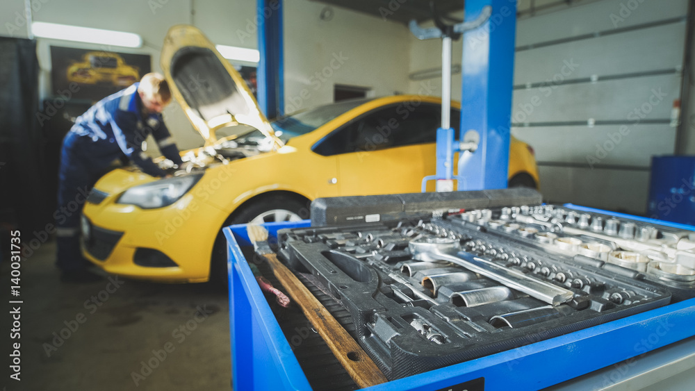 Defocused - a worker mechanic checks the electrical in the hood of the yellow car, garage workshop