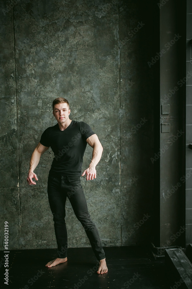 Young sexy men bodybuilder athlete, studio portrait loft on background of stylized Concrete brutal wall, guy model black Tshirt and trousers