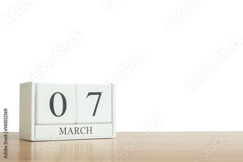 Closeup surface white wooden calendar with black 7 march word on blurred brown wood desk isolated on white background with copy space , selective focus at the calendar