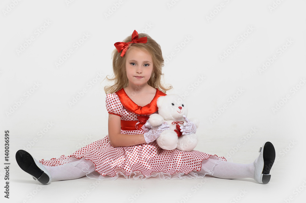 Lovely little girl in a very short white summer dress sits on her knees on  the floor and hugging a Teddy bear . Stock Photo