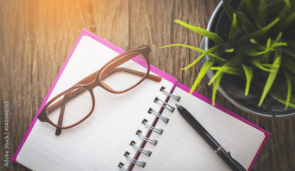 Glasses, pen and opened notebook on wooden table with flowerpot from top view point Glasses, pen and opened notebook on wooden table with flowerpot from top view point