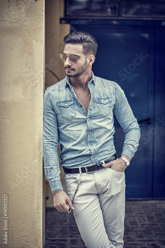 Attractive young man standing against colorful wall, looking to a side, wearing denim shirt