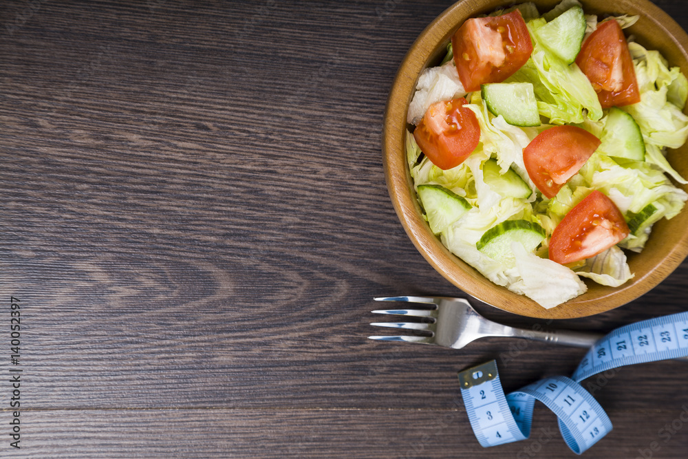 Salad in wooden bow,forkl and measuring tape on a table close-up.