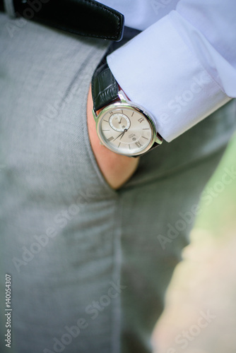 Man with steel watch holds hand in pocket of grey trousers