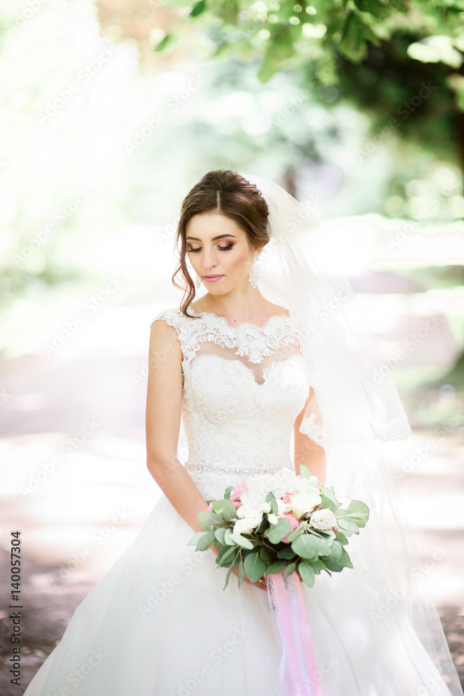 Bride in magnificent dress closes her eyes posing with wedding bouquet in the park Bride in magnificent dress closes her eyes posing with wedding bouquet in the park