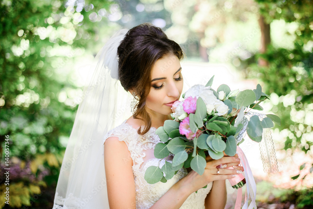 Stunning bride in long veil poses in arch of green branches Stunning bride in long veil poses in arch of green branches