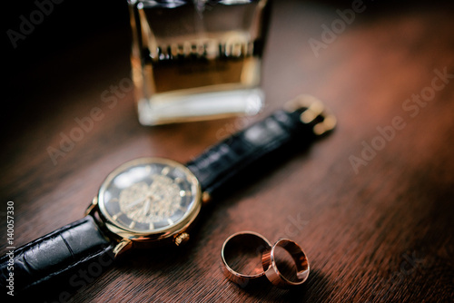 Golden cufflings, wedding rings and watch lie on wooden table
