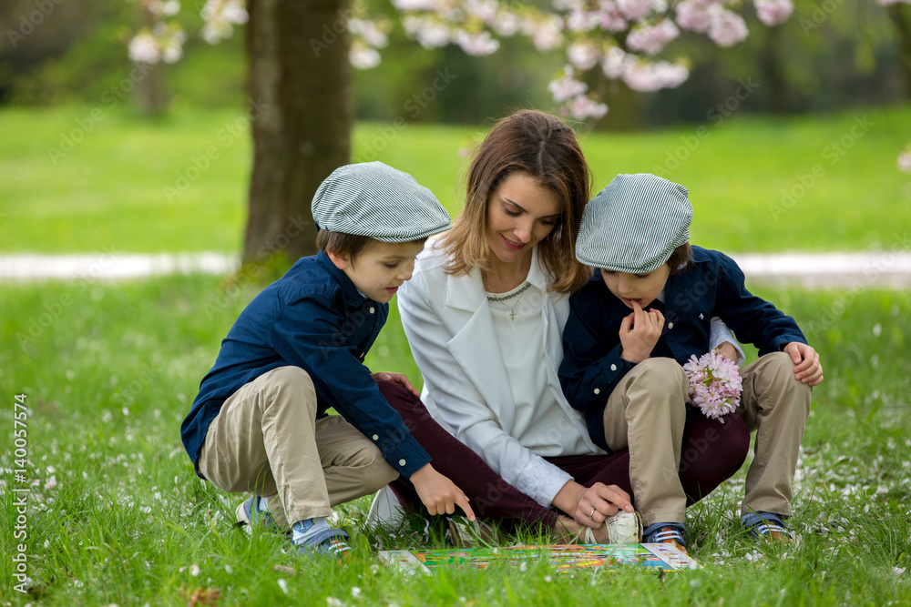 Mother with two children, boys, reading a book in a cherry blossom garden Mother with two children, boys, reading a book in a cherry blossom garden