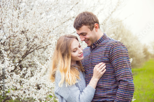 Young romantic couple standing in front of wonderful blooming trees in spring garden