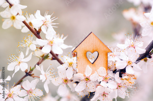 Wooden house with hole in form of heart surrounded by flowering branches of spring trees