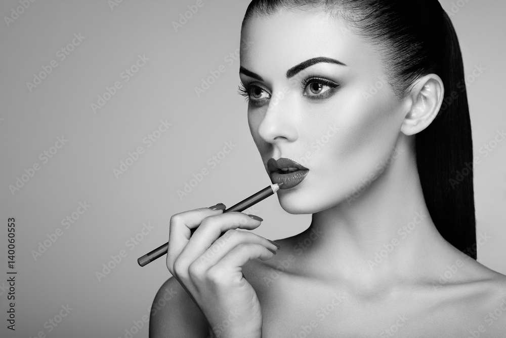 Obraz premium Black and white photo of woman painting lipstick. Beautiful woman face. Makeup detail. Beauty girl with perfect skin. Red lips and nails manicure