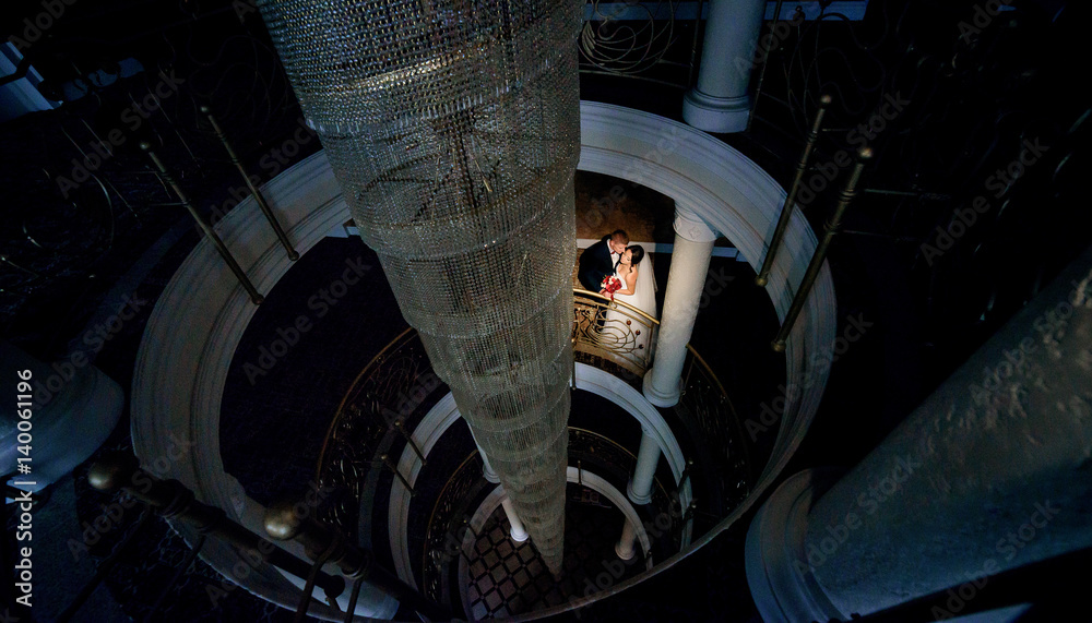 Fototapeta premium Look from above at wedding couple standing on spiral stairs