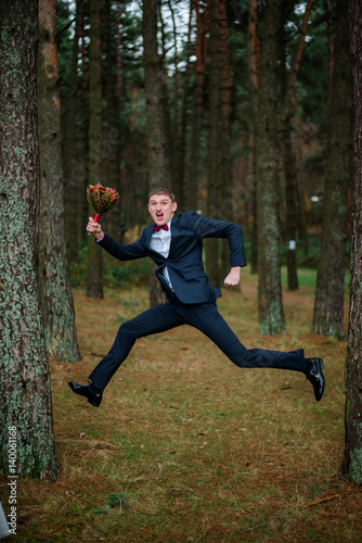 Funny groom jumps with bouquet in the forest