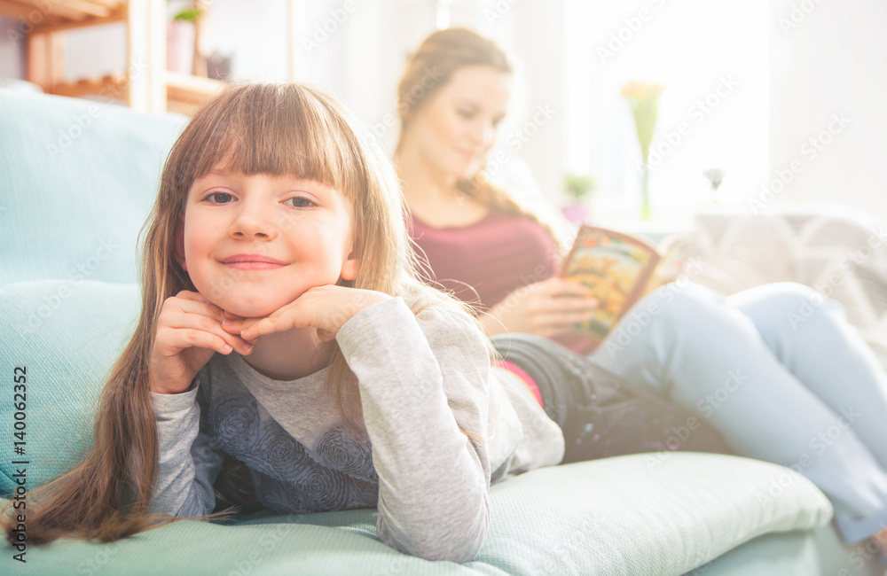 Mother and daughter sitting on sofa and reading book Mother and daughter sitting on sofa and reading book
