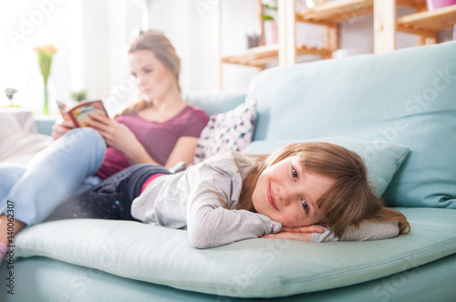 Canvas-taulu Mother and daughter sitting on sofa and reading book